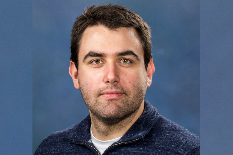 Ludmil Alexandrov head and shoulders looking at camera wearing a dark blue jumper on a light blue background